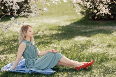 Portrait of a beautiful young blonde woman who sits under a flowering tree and enjoys spring