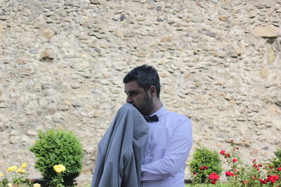 Thoughtful man holding suit while standing against wall