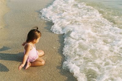 High angle view of girl kneeling on shore at beach