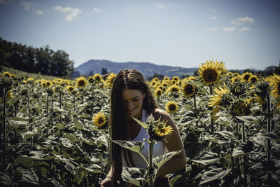 Woman standing at sunflower farm against sky