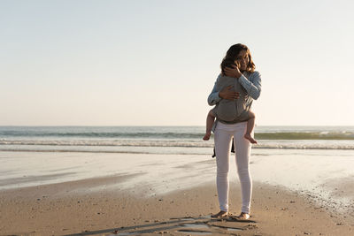 Mother carrying son while standing at beach