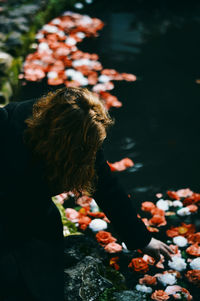 Side view of woman reaching flowers in lake