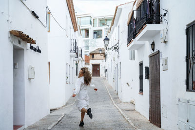 Rear view of woman in white dress running on street