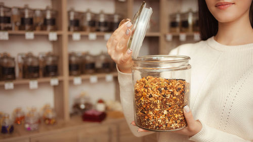 Woman salesman at tea shop smiles, offers goods. natural chinese tea in glass jars.