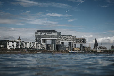 View of buildings by river against cloudy sky