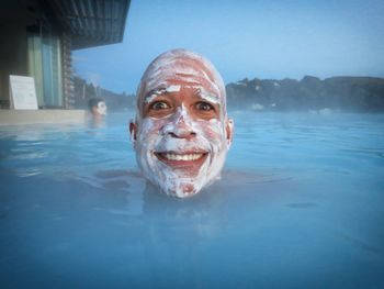 Portrait of cheerful man with mud mask in blue lagoon