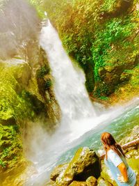 Rear view of woman looking at waterfall in forest