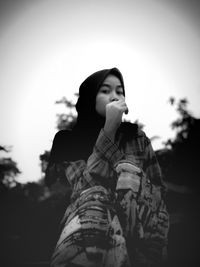 Low angle portrait of young woman standing against sky