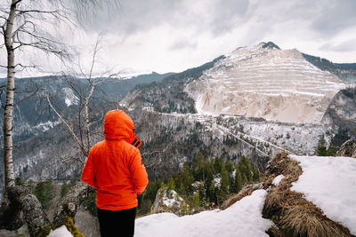 Rear view of man standing on snowcapped mountain against sky