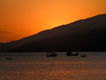 Silhouette boats on sea against orange sky