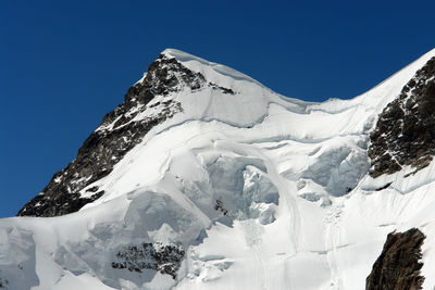 Low angle view of snowcapped mountains against clear blue sky