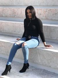 Portrait of young woman sitting on staircase against wall