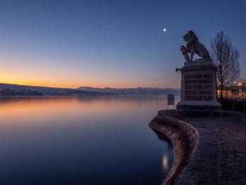 Statue by lake against sky during sunset