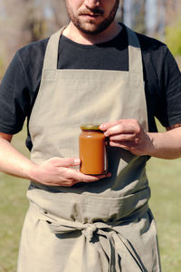 Unrecognizable crop male farmer standing in village with glass jar of tasty honey