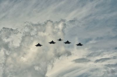 Low angle view of silhouette fighter planes flying in cloudy sky