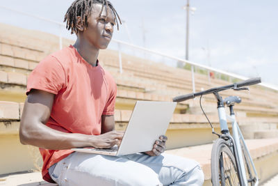 Ethnic guy using laptop near bicycle