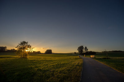 Road amidst field against clear sky during sunset