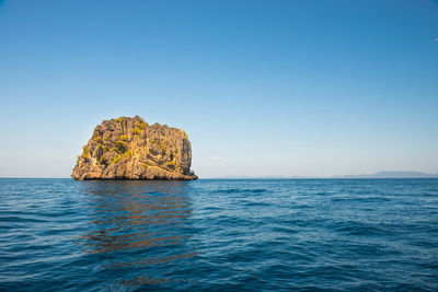 Rock formation in sea against clear blue sky