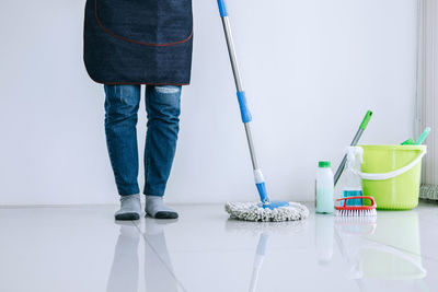 Low section of cleaner standing with mop on tiled floor against wall