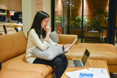 Young woman using phone while sitting on sofa at home