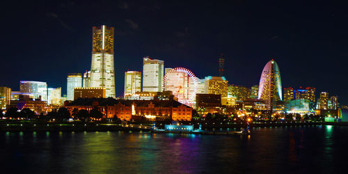 Illuminated buildings by river against sky at night