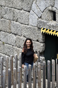 Portrait of smiling woman standing on footbridge against wall