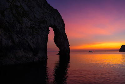 Silhouette rock formation in sea against sky during sunset