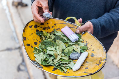 Midsection of person holding coca leaves and cigarettes in plate