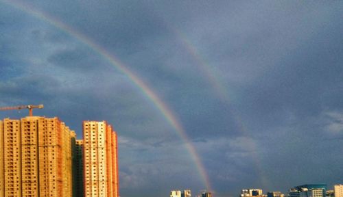 Low angle view of rainbow over buildings against sky
