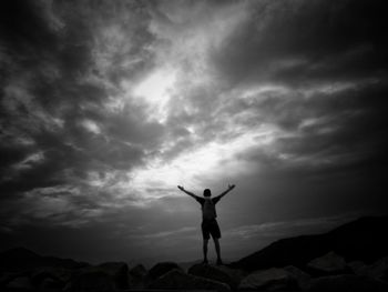 Silhouette man standing on arms outstretched against sky at sunset