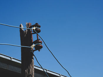Low angle view of bird perching on cable against clear blue sky