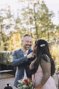 Happy mature groom looking at young bride holding bouquet during wedding