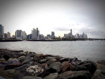 View of calm river in front of cityscape against sky