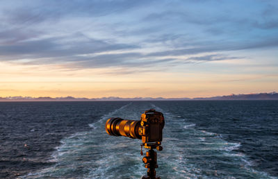 Rear view of woman photographing sea against sky during sunset