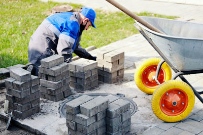 Bricklayer in work clothes sits on sidewalk and lays out paving slabs. sight of working man in open