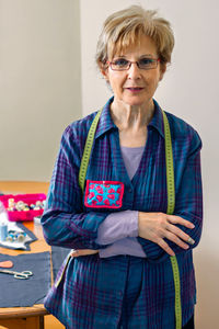 Senior dressmaker posing looking at camera with table with sewing materials in the background