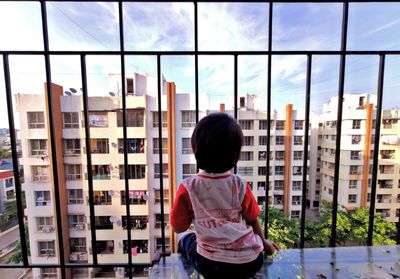 Rear view of boy looking through window