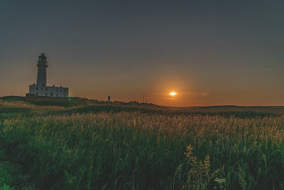 Lighthouse on field against sky during sunset