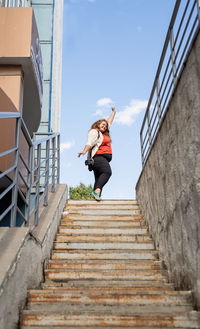 Low angle view of woman walking on staircase against sky