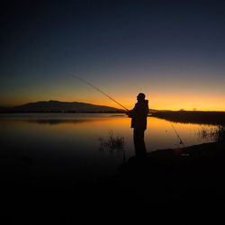 Silhouette man fishing at sunset