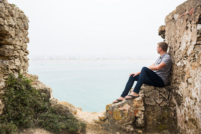 Side view of young man sitting on rock