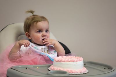 Cute baby girl eating birthday cake while sitting on high chair at home