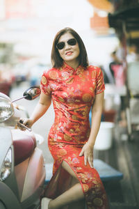Portrait of smiling mature woman wearing traditional clothing and sunglasses while standing by motor scooter in city