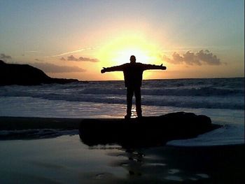 Silhouette man with surfboard standing at beach during sunset