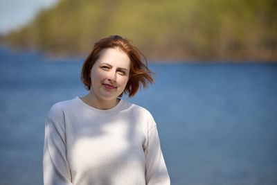 Portrait of young woman standing against lake