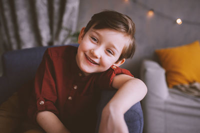 Portrait of smiling cute boy sitting on chair at home