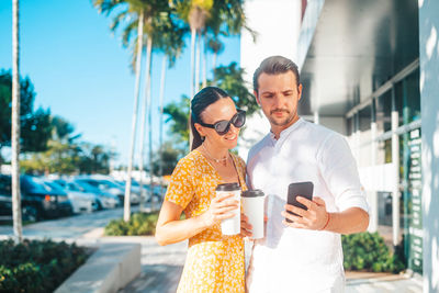 Portrait of smiling young woman using mobile phone while standing in city