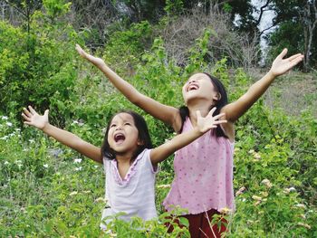 Happy siblings standing with arms raised amidst plants on field