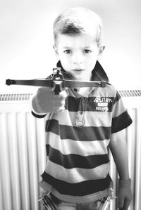 Portrait of smiling cute boy holding toy while standing against radiator at home