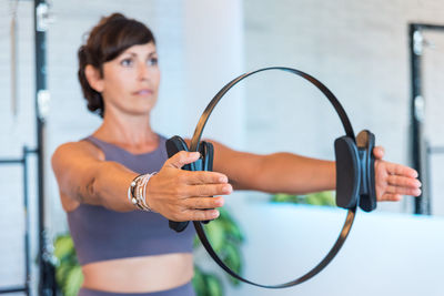 Delighted adult woman in sportswear and exercising with ring in outstretched arms during pilates training in gym